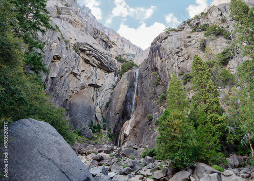 Rocky canyon floor and tall waterfall descending from granite cliffs, Yosemite National Park, California, USA