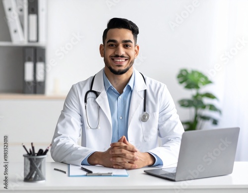 A doctor in a white coat is sitting at a table in the office, smiling and looking at the camera.