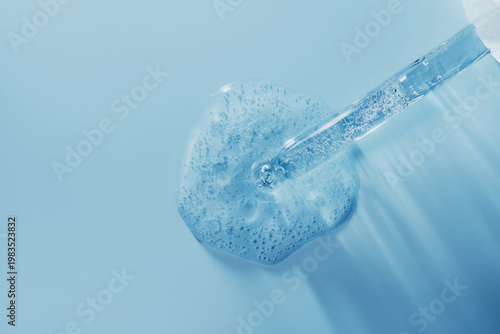 Pipette dripping transparent blue gel serum on blue background, perfect for skincare and cosmetic concepts