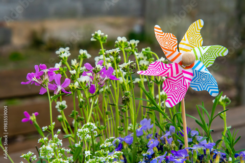 Foto Colorful toy pinwheel in flower pot with blooming spring flowers, vibrant garden decoration with purple and white blossoms, cheerful backyard scene with spinning windmill and floral arrangement