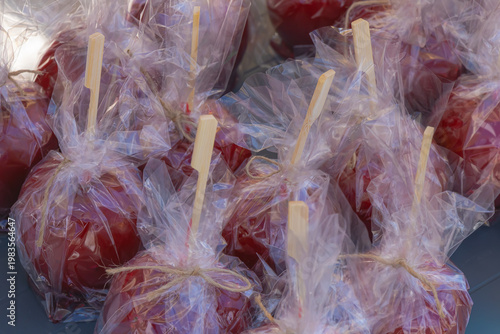 Fotografie Candied apples wrapped in clear plastic with wooden sticks at market stall festi