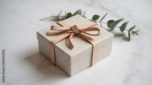 Elegant light beige gift box with brown ribbon on white marble surface