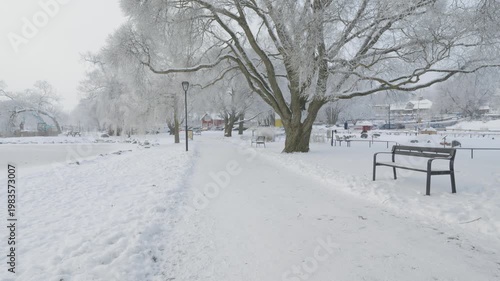 A tranquil pathway winds through a snow-covered landscape, lined with trees. The scene captures the stillness and beauty of winter, inviting a sense of peace and solitude amid the cold.