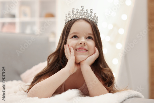 Photos Beautiful little girl with crown dreaming about becoming queen on bed at home