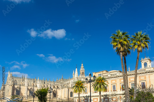 Seville, Andalusia, Spain, a beautiful low-angle view showcasing the magnificent gothic architecture of the Seville Cathedral, alongside the historic Archivo General de Indias building and palm trees