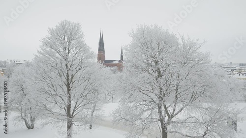A serene winter scene featuring frosted trees and church steeples emerging from a snowy landscape. The tranquil atmosphere invites a sense of calm and reflection amidst the white, picturesque surround