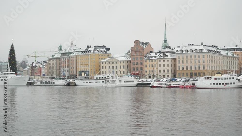 A picturesque winter scene featuring a snowy waterfront lined with colorful buildings and boats. The serene atmosphere showcases the beauty of a winter day, highlighting architectural structures refle