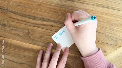 Close up of hands writing “I love you dad” on small card, heartfelt Father’s Day message with simple handwritten text, natural light overhead shot on wooden table, 4K video