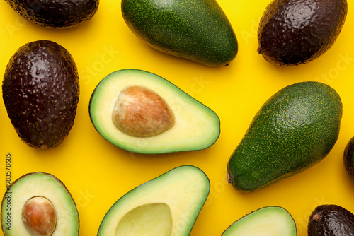 Whole and cut fresh avocados on yellow background, flat lay