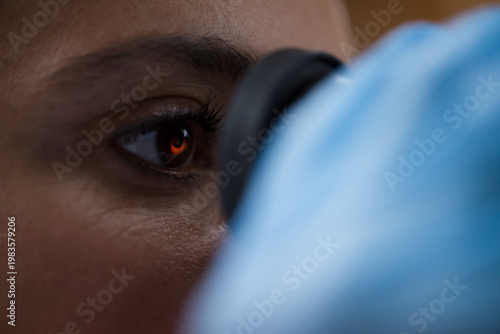 Young doctor examining blood sample through microscope eyepiece in medical testing laboratory