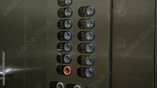 Hand presses illuminated elevator button on metal control panel, closeup of numbered buttons and glowing indicator, tactile