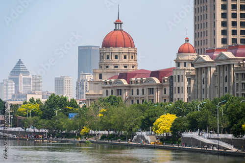 A picturesque view of the Hai River in Tianjin featuring a blend of classical European-style architecture and modern skyscrapers along the sunlit waterfront. China, 22 May 2025