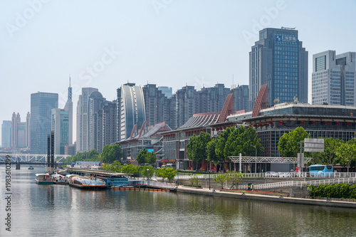 The Hai River flows through the heart of Tianjin, flanked by a mix of modern skyscrapers and green riverside promenades reflecting in the calm water. China, 22 May 2025
