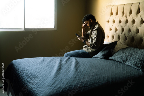 Man feeling worried on bed with device