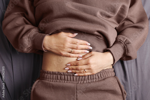 Woman holding stomach with pain gesture. Health problem concept showing abdominal discomfort. Close view of hands on belly indicating illness, digestion issue or cramps in lifestyle context.