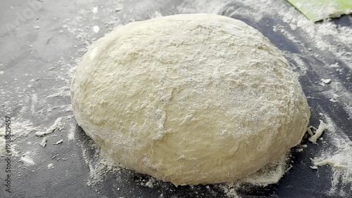 Dough ball being prepared on a black surface with flour scattered around, showcasing the texture and consistency of the mixture in a kitchen setting