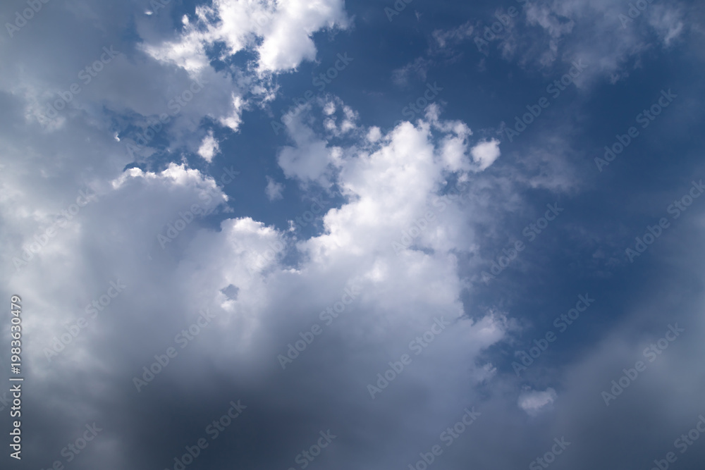 Fototapeta premium Dramatic cumulus clouds gather over a deep blue sky, contrasting bright white tops and dark storm shadows, suggesting changing weather, moodiness, and the power of nature.