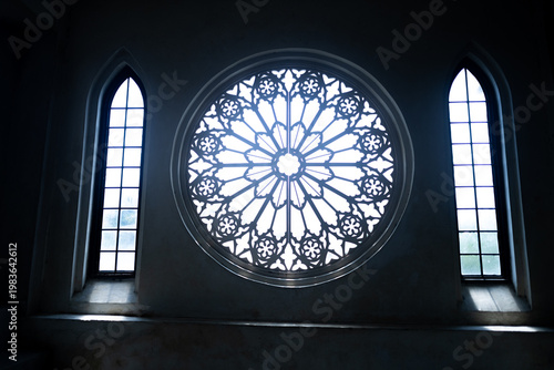 Slika na platnu Beautiful Ornate circular stained glass style window inside a dark Gothic church interior between two pointed cathedral windows