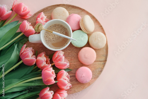 Bouquet of pink tulips, cup of coffee and macaroons on pink background. Mothers day celebration concept.