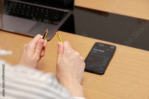 A person holds a broken pencil in both hands, symbolizing frustration, stress, or worry about financial losses or poor investment decisions. The setting appears to be a work desk, reinforcing the idea