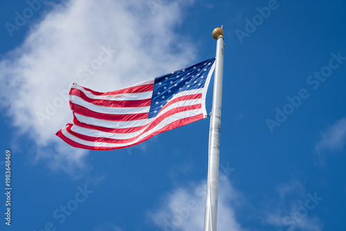 American flag waving on flagpole against blue sky with clouds