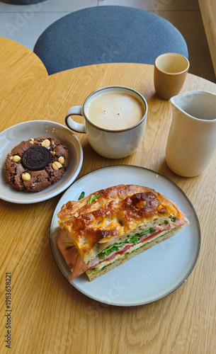 Wooden table holds breakfast: coffee, milk, cookie, and sandwich