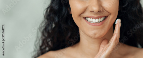 Foto A woman with curly hair smiles while placing her hand on her cheek