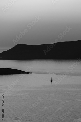Beautiful view of a sailing boat next to the volcano Palea Kameni in Santorini Greece in black and white