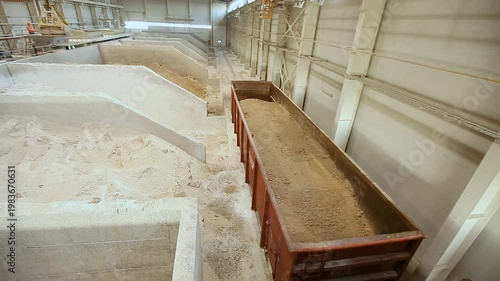 Unloading of open wagons and storage of bulk materials in a industrial warehouse. The interior of a factory clay and sand warehouse. Unloading wagons of clay at the warehouse. Bulk cargo. Unloading