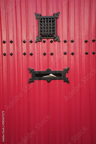 Altes rote Haustür mit traditionellem Sprechgitter in der Fassade aus rotbraunem Backstein eines Altbau bei Sonnenschein in den Gassen der Altstadt von Brügge in 