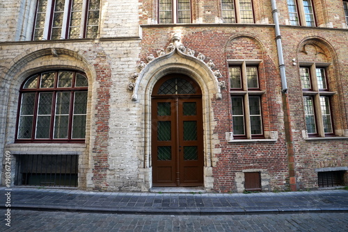 Prachtvoller alter Hauseingang mit Rundbogen in der Fassade aus Backstein eines Altbau mit Kopfsteinpflaster bei Sonnenschein in den Gassen der Altstadt von Brügge in Westflandern in Belgien