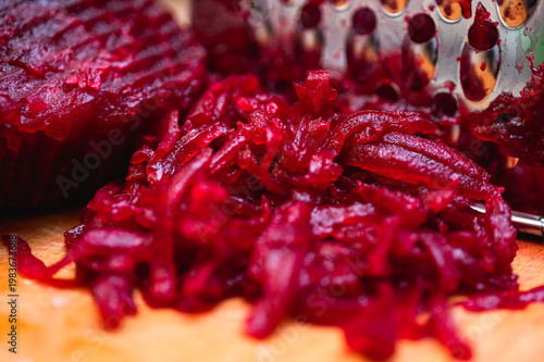Macro of boiled red beetroot being grated on a metal grater on a wooden board. Healthy cooking process for salad or borscht. Vibrant magenta vegetable food texture