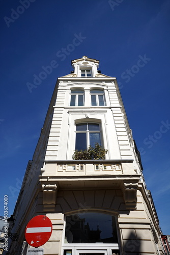 Weiße schmale sanierte alte Fassade mit Sprossenfenster bei blauem Himmel und Sonnenschein eines Eckhaus in der Altstadt von Brügge in Westflandern in Belgien	

