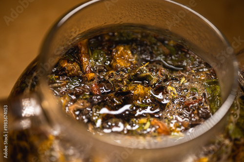 Macro shot of brewing herbal tea in a glass teapot. Natural organic infusion of tea leaves and dried flowers. Wellness, relaxation and healthy lifestyle concept