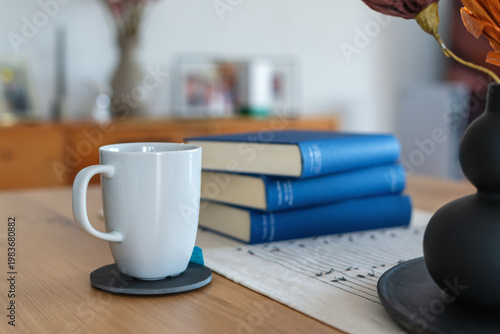Photos White cup of tea and three blue books on wooden table at home