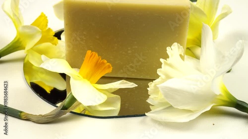 A bar of soap, fresh flowers daffodil reflected in the mirror on a white background, cosmetics based on daffodils, side view