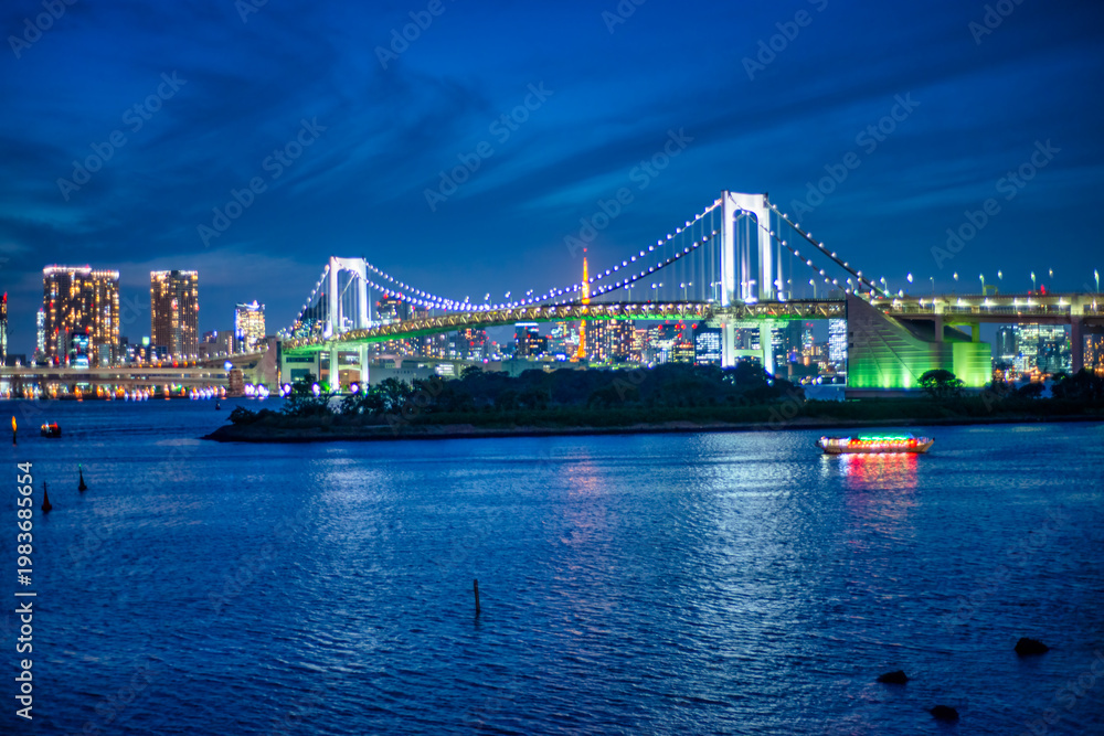 Fototapeta premium Illuminated Rainbow Bridge at night in Odaiba, showcasing Tokyo’s iconic architecture and colorful urban skyline