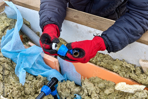 Plumber inserting compression ring into compression nut during repair of HDPE distribution piping in well pit.