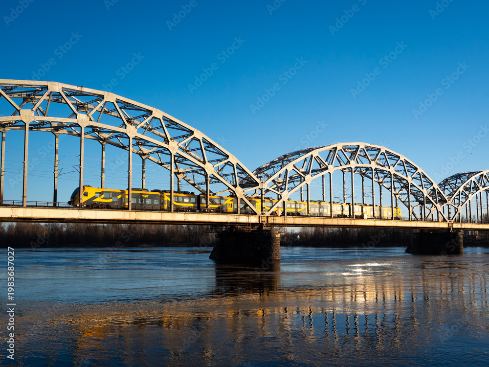Fototapeta premium A yellow train crosses an arched bridge over the river