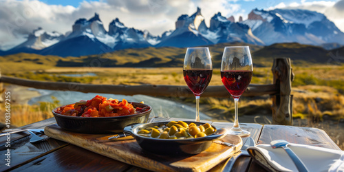 Traditional Chilean food served with glasses of red wine on an outdoor table overlooking the dramatic peaks of Torres del Paine