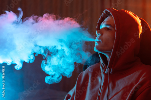 young man exhales a cloud of steam or smoke in colored lighting