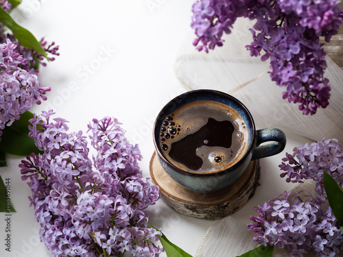 Coffee cup on a wooden stand on a white table with blooming lilac branches. Copy space