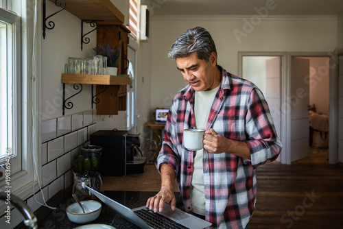 Foto Middle-aged man working on laptop in home kitchen