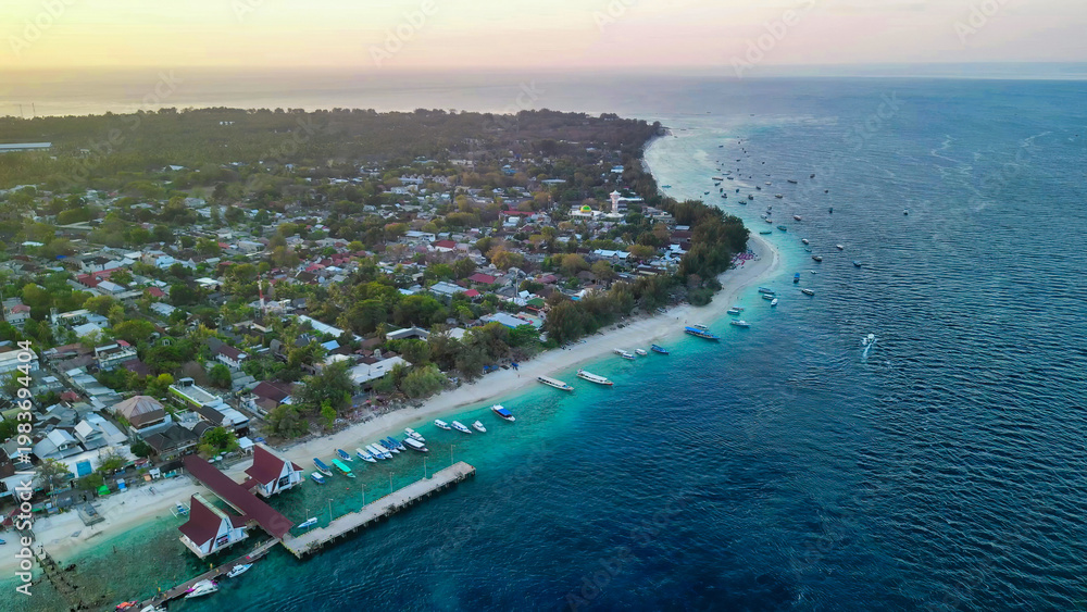Fototapeta premium Aerial drone view of Gili Trawangan island at sunset showing golden sky, Mount Agung silhouette, and turquoise waters Indonesia