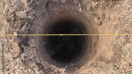 Deep round holes for fence posts, surveyor marking layout with yellow string, landscaper clearing loose soil, contractor preparing.