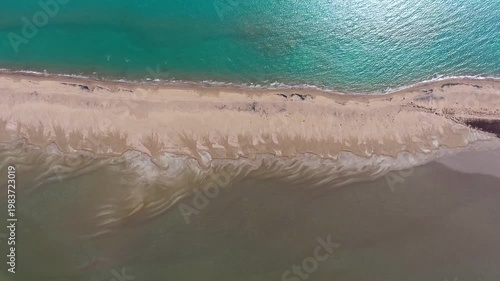 Aerial view of long thin sand tombolo separating turquoise sea and calm coastal lagoon landscape. This natural formation shows sandy barrier dividing open water shallow lake area in goksu delta.