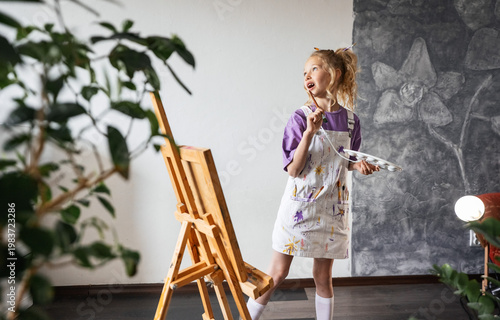 Cute girl painting picture on canvas in bright room. Artistic process, imagination and creativity. Concept of hobby, talent development and relaxed home atmosphere. Art lessons