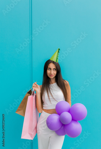 Happy young woman holding several paper shopping bags against a turquoise background. 