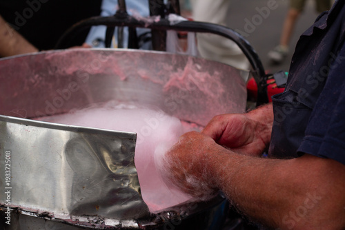 Horizontal photo close up. Man seller behind street sweets counter, pastry shop, stall makes and sells pink cotton candy in machine. Independence day, May 26, 2025. City festival Tbilisoba, fair, sale