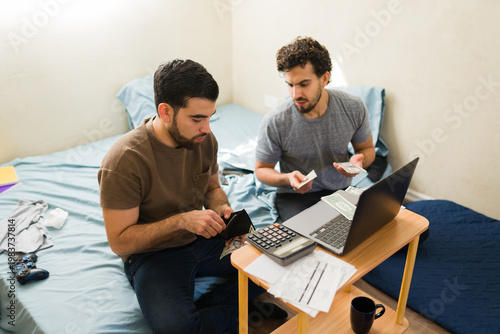 Latin men budgeting and calculating finances, managing household bills while counting money in their first apartment